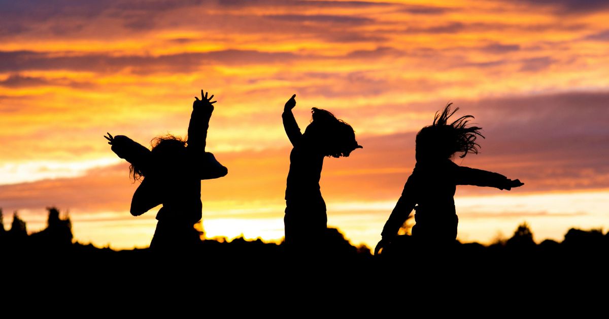 Silhouettes of children jumping and moving at sunset, expressing joy, rhythm, and a return to embodied motion.