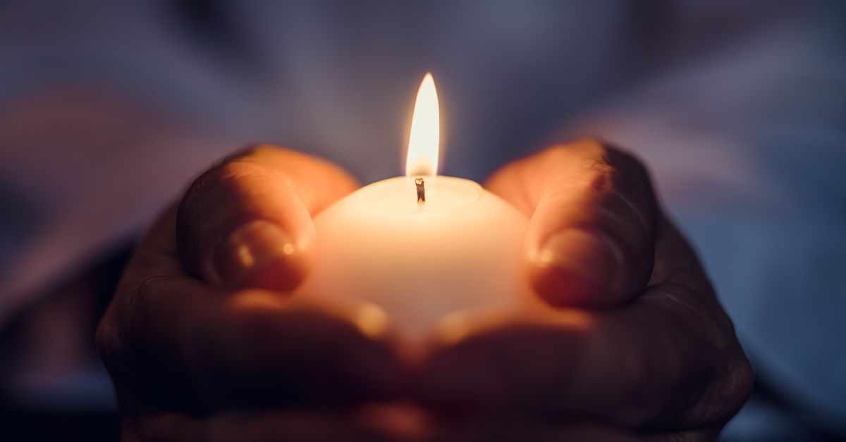 Hands holding a lit candle in darkness for “The Candle Between Us”