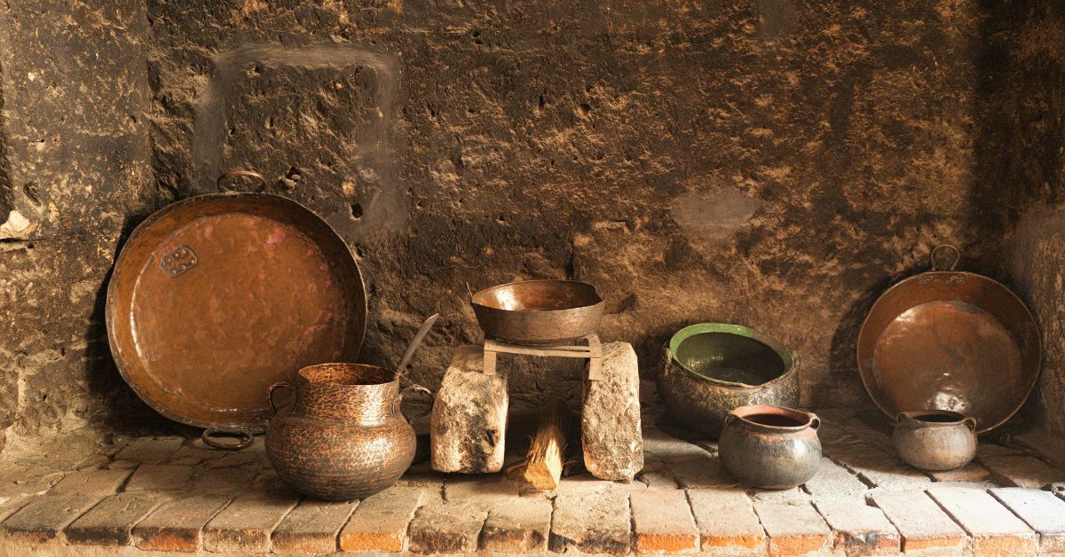 Rustic hearth with old copper pots and stone supports for “The Hearth as Sanctuary”