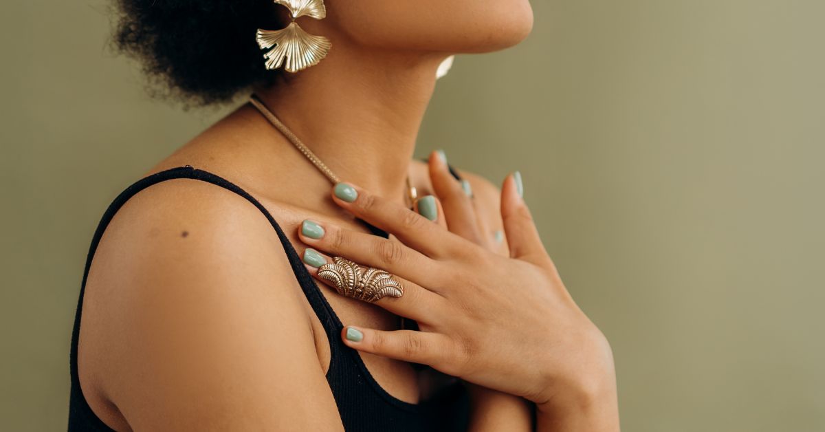 Person with hands resting on their chest, wearing natural jewelry, expressing embodied listening, presence, and self-attunement.